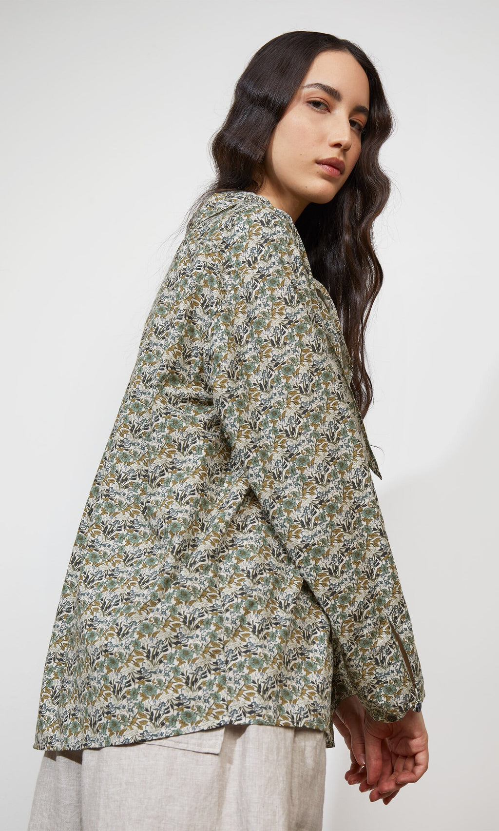 Plümo- Woman with long dark hair wears the Garden Blouse, posing in beige pants against a plain background.