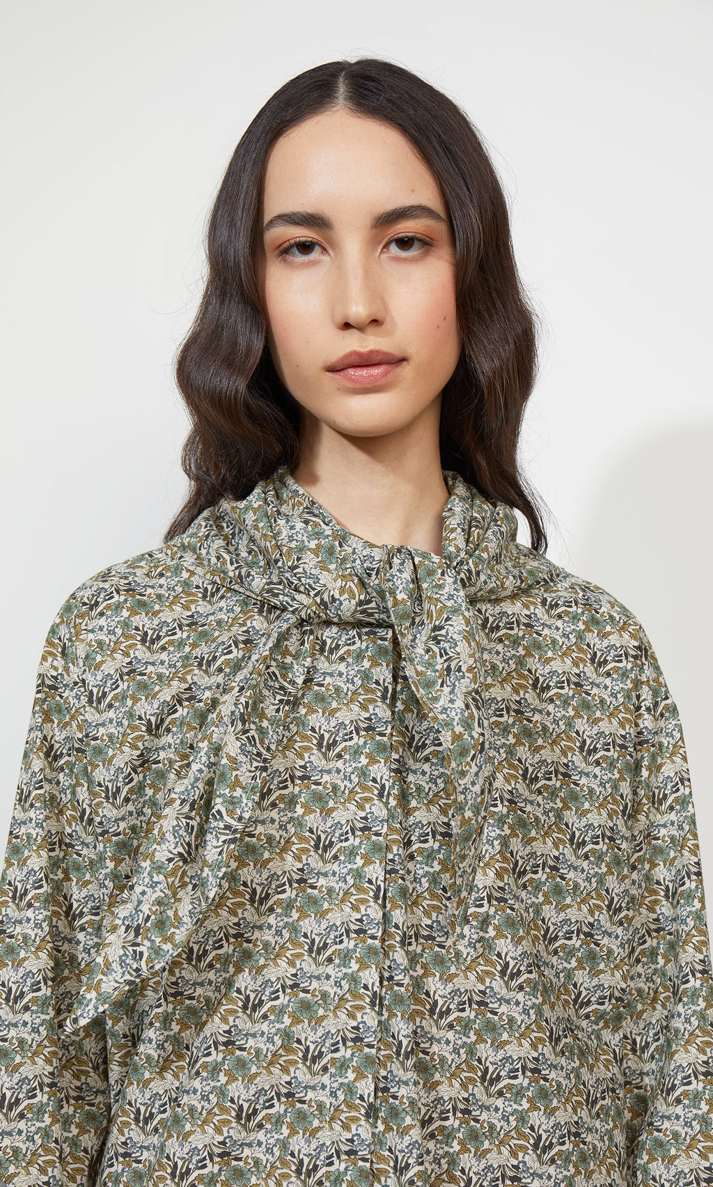 Plümo- Woman with long wavy hair wears the Garden Blouse with a large neckerchief tie, looking at the camera.