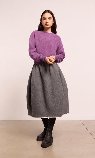 Plümo  Person in the Wicklow Crewneck - Heather, gray skirt, and black boots stands on a beige floor with light background.