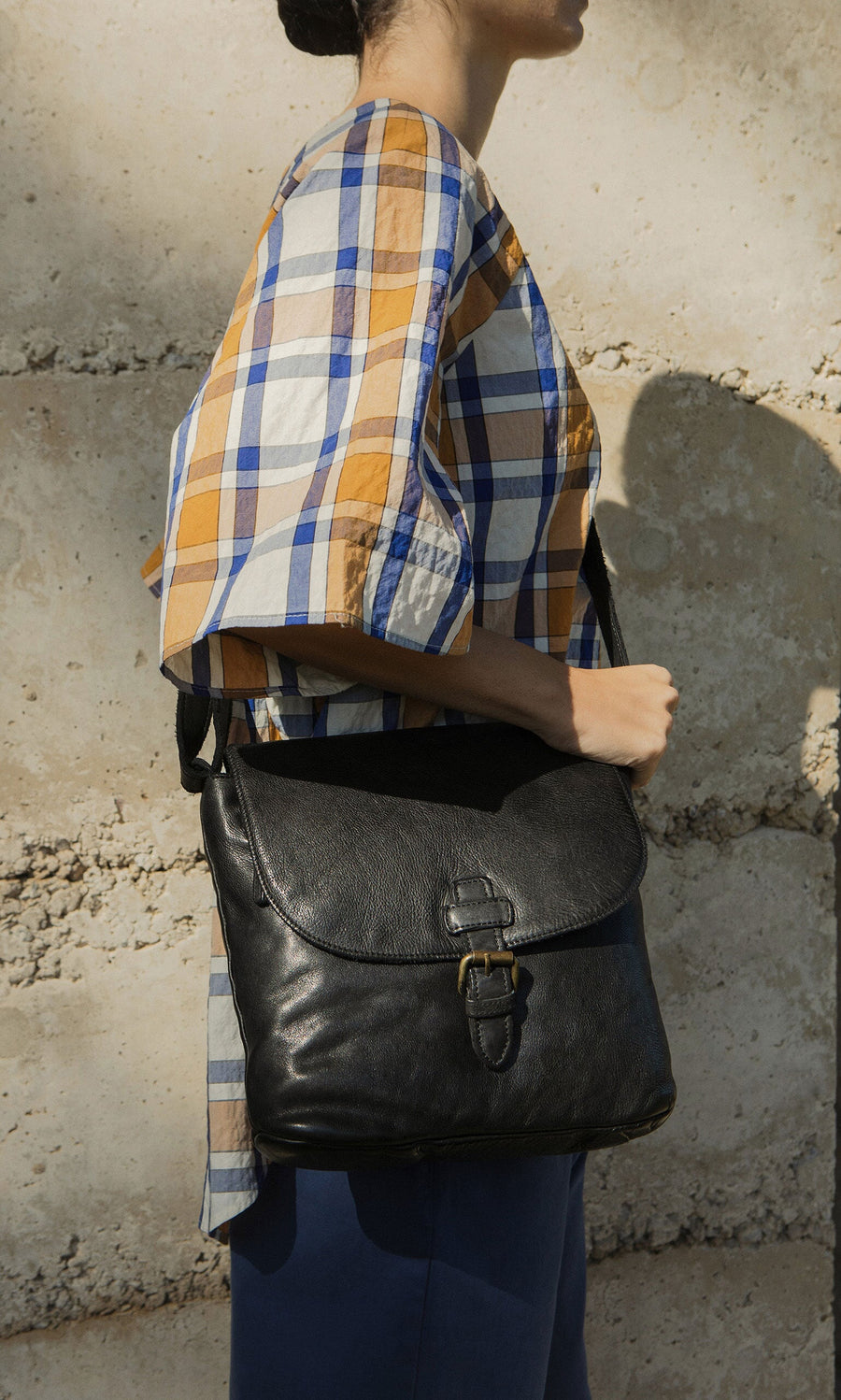 Plümo- Person in a plaid shirt and blue pants carries the Beck Crossbody Bag with an adjustable strap in sunlight.