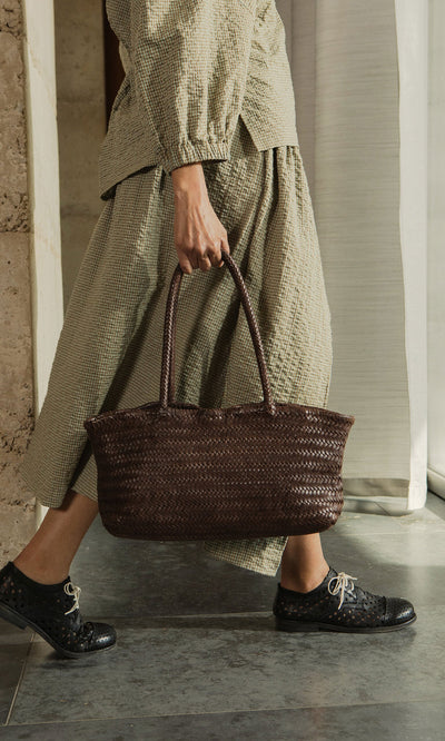 Plümo- Person walking indoors in a checked outfit and black shoes, carrying the chic Inga Plait Bag.
