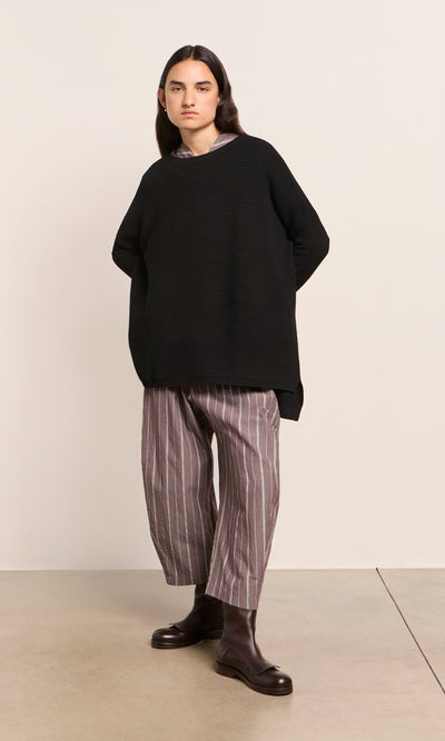 Plümo  Person in a Jack Sweater - Black, striped wide-leg pants, and brown boots stands against a plain background.
