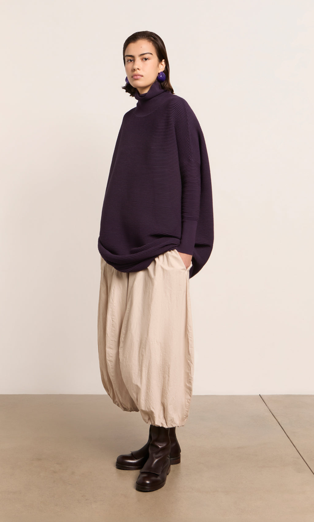 Plümo  Person wears a Longer Jack Rollneck - Lupin, beige balloon pants, and black boots against a plain light background.