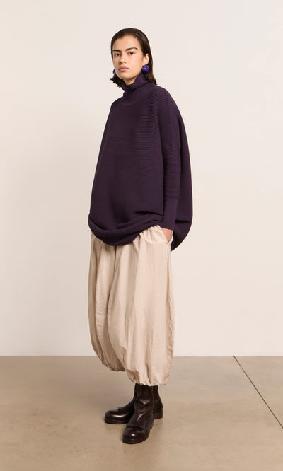 Plümo  Person wears a Longer Jack Rollneck - Lupin, beige balloon pants, and black boots against a plain light background.