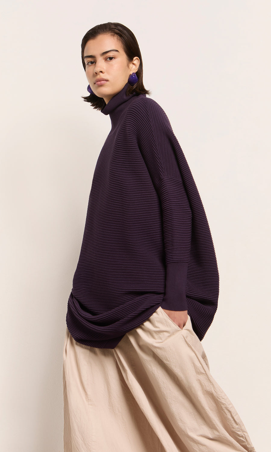 Plümo  Person wears Longer Jack Rollneck - Lupin and beige skirt, standing against a plain light background.