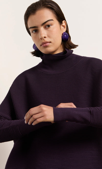 Plümo  Person in the Longer Jack Rollneck - Lupin sweater with bold earrings, standing against a light background.