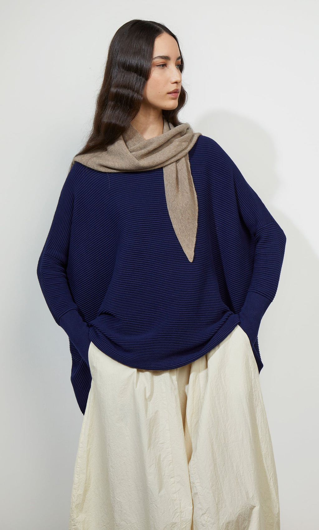Plümo- Woman in the Jack Sweater - Navy, with dropped shoulders, cream skirt, and scarf, standing against a white background.