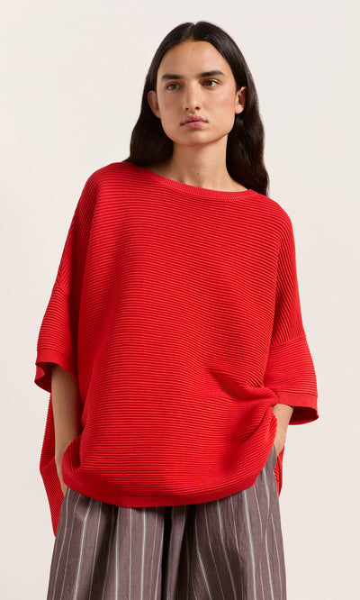 Plümo  Person wears Jack Sweater Short Sleeve in Lava, hands in pockets, standing against a light background.
