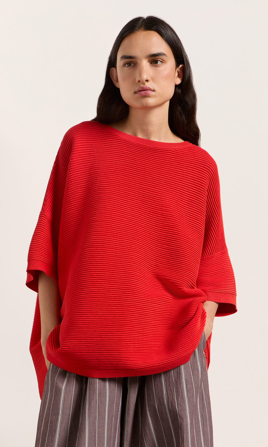 Plümo  Person wears Jack Sweater Short Sleeve in Lava, hands in pockets, standing against a light background.