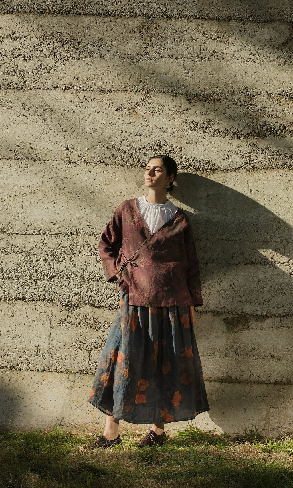 Plümo- A person in the Jia Wrap Top stands against a textured wall in sunlight, casting a shadow.
