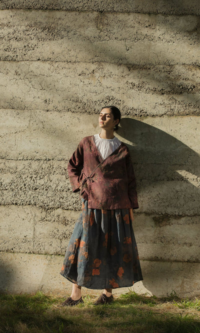 Plümo- A person in the Jia Wrap Top stands against a textured wall in sunlight, casting a shadow.