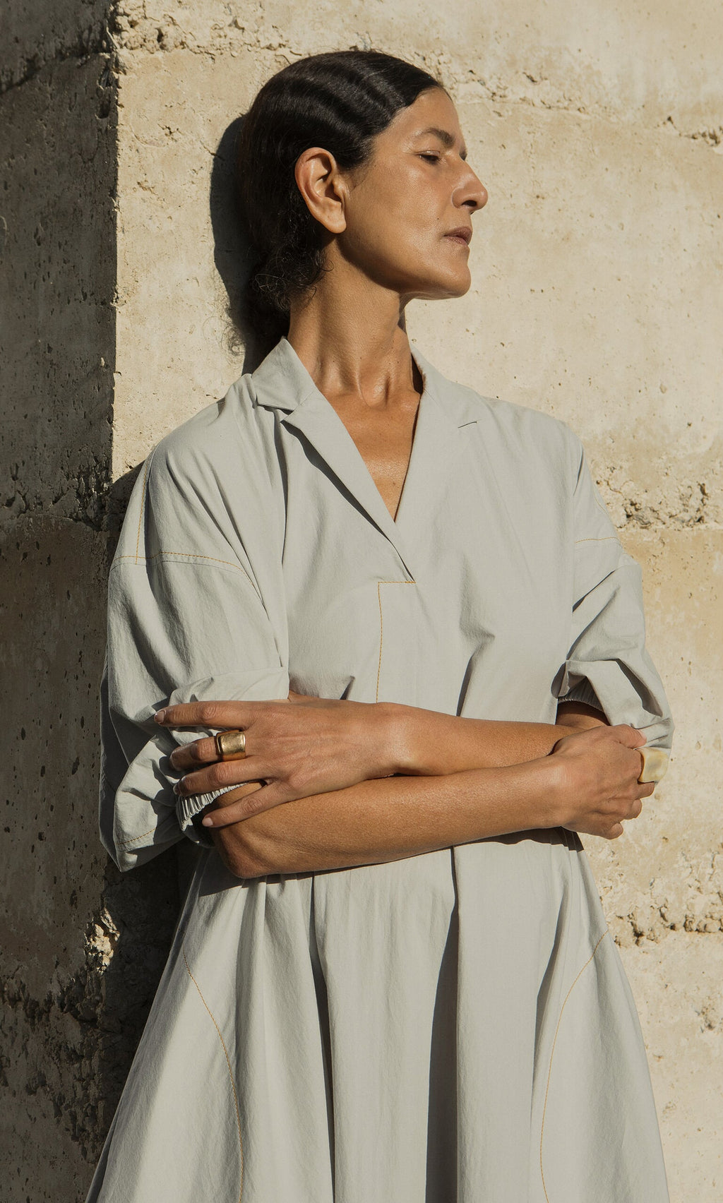 Plümo- A woman in the Kaisa Dress with balloon sleeves stands against a stone wall, eyes closed and arms folded.