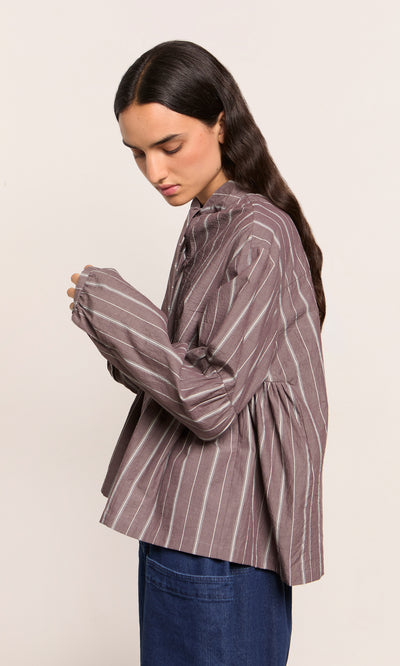 Plümo  Person in Kleist Blouse - Liquorice with blue jeans, facing sideways against a plain background.