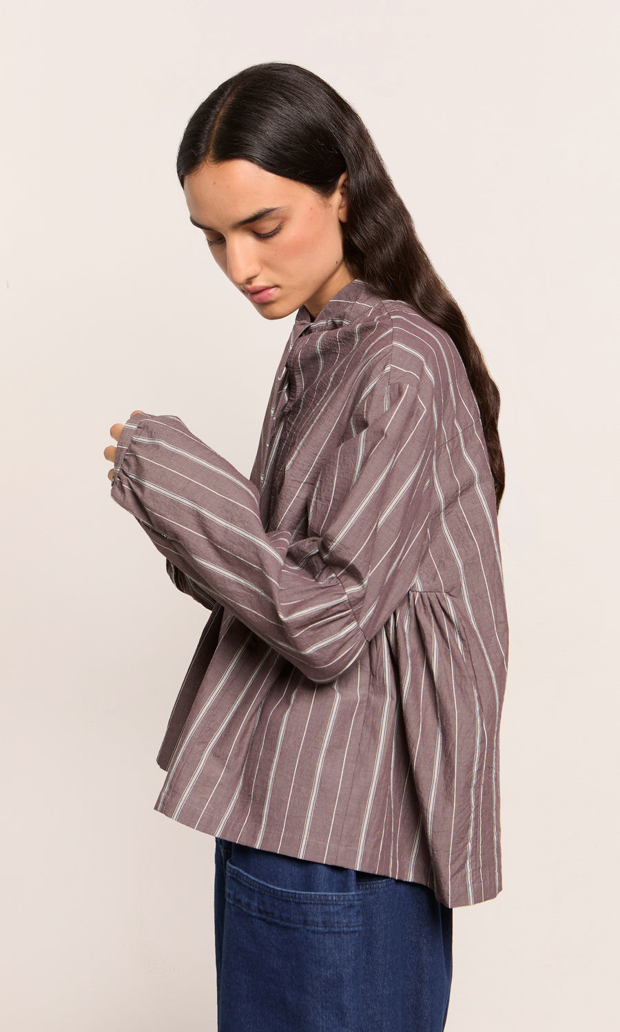 Plümo  Person in Kleist Blouse - Liquorice with blue jeans, facing sideways against a plain background.