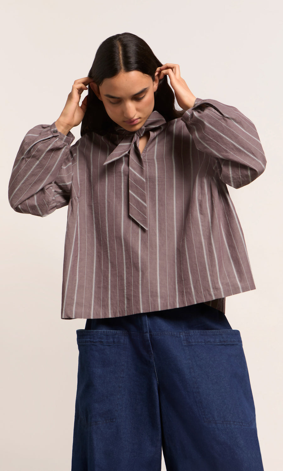 Plümo  Person in the Kleist Blouse - Liquorice by Plümo Studio, wide-leg pants, looking down and adjusting their hair.