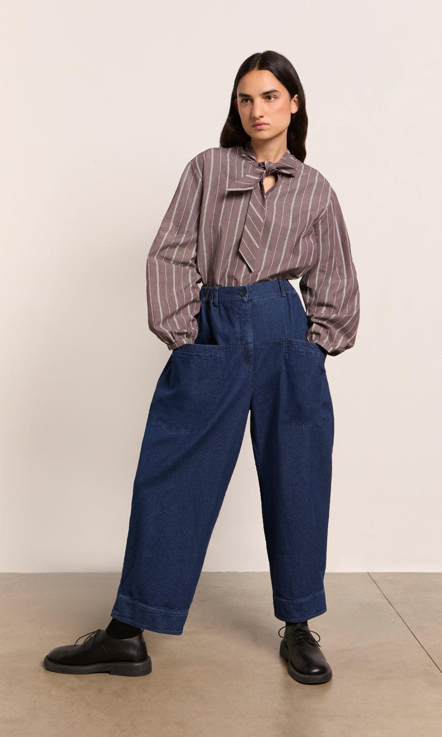 Plümo  Person in a Kleist Blouse - Liquorice, blue wide-leg pants, and black shoes stands against a plain background.