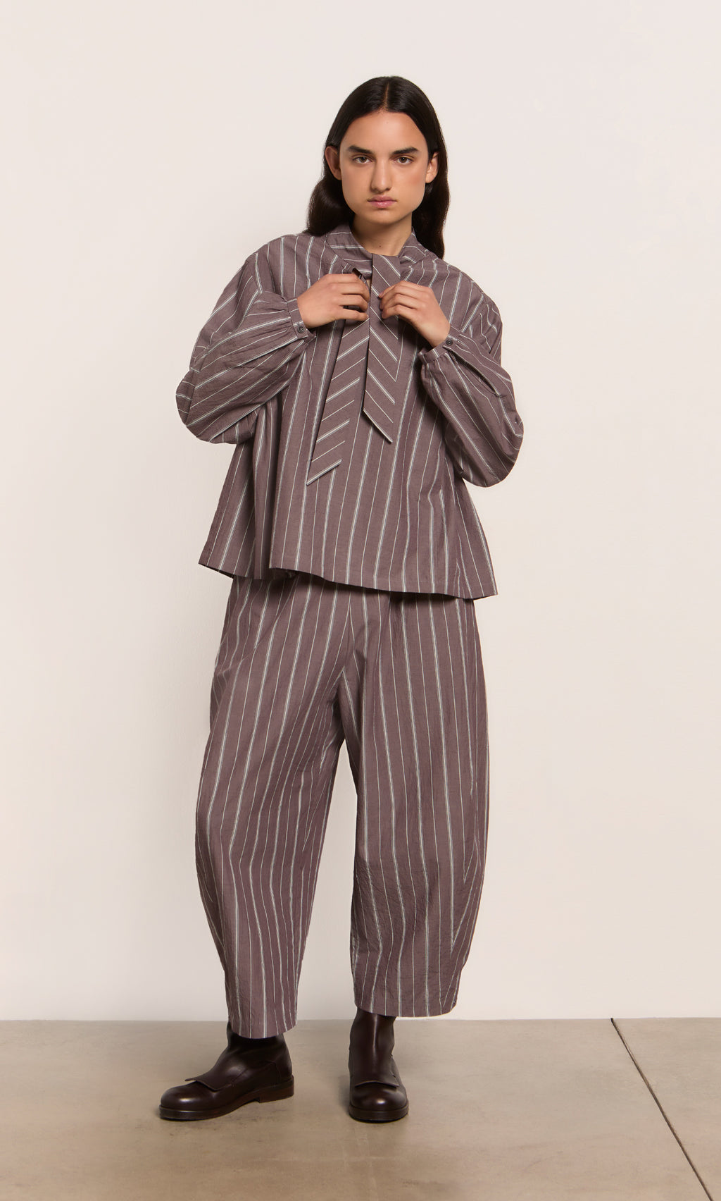 Plümo  Person in Butoni Pants - Liquorice: loose, striped cotton pants with elastic waist, styled seriously.