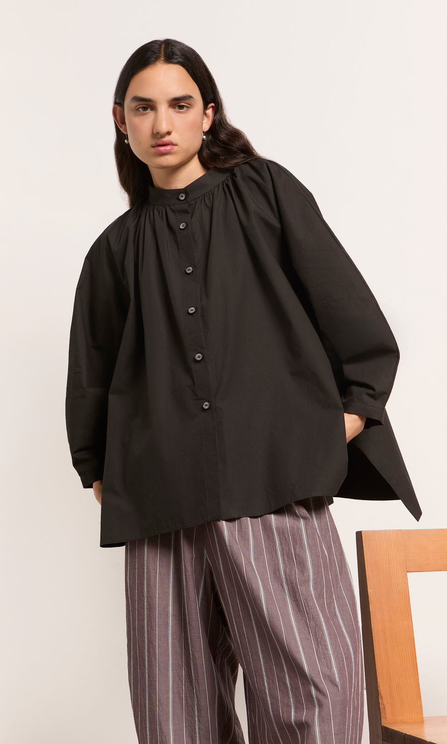 Plümo  Indoors, a person wears the Kroyer Blouse in black with brown wide-leg pants featuring white stripes.