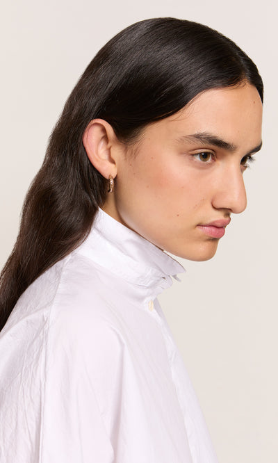 Plümo  Person with long dark hair wears Leaping Fish Hoops and a white shirt, shown in side profile against a plain background.