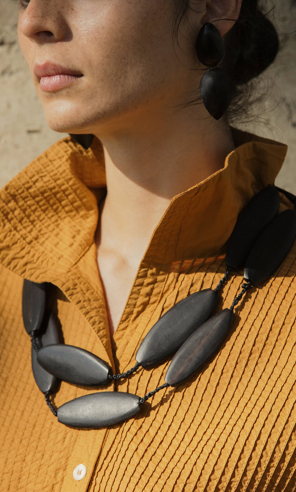 Plümo- Woman in a textured mustard shirt wears the Benin Necklace, showcasing unique handmade African jewelry.