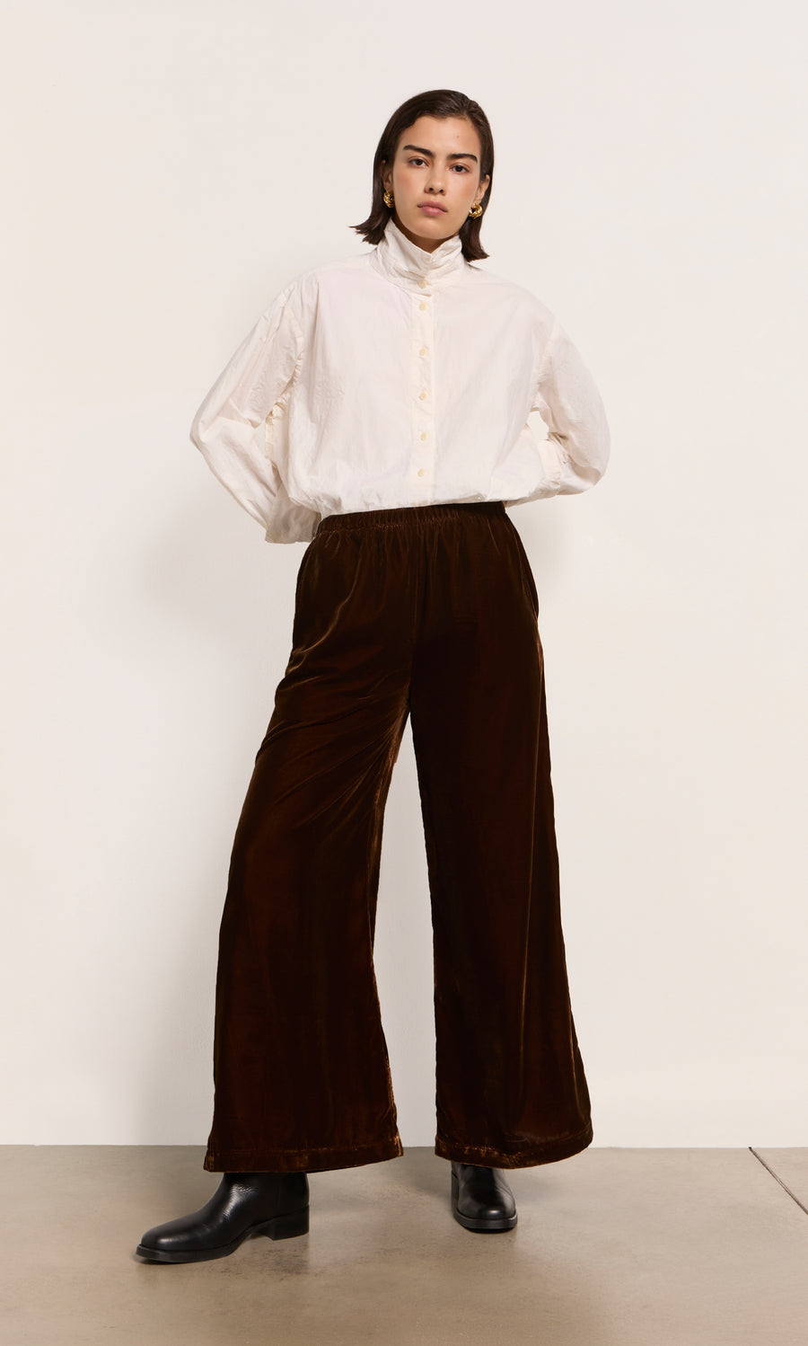Plümo  Person in a white button-up shirt, Maroon Velvet Pants with wide legs, and black boots.