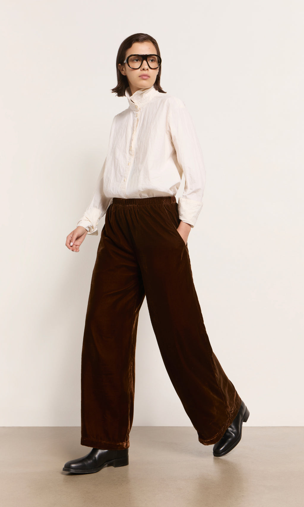 Plümo  Person wears a white shirt, Maroon Velvet Pants, and black boots, standing against a plain background.