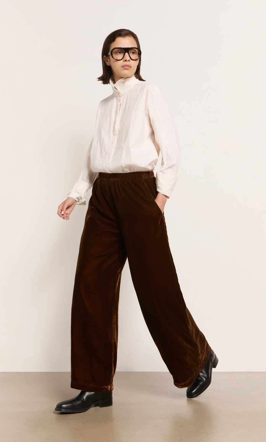 Plümo  Person wears a white shirt, Maroon Velvet Pants, and black boots, standing against a plain background.