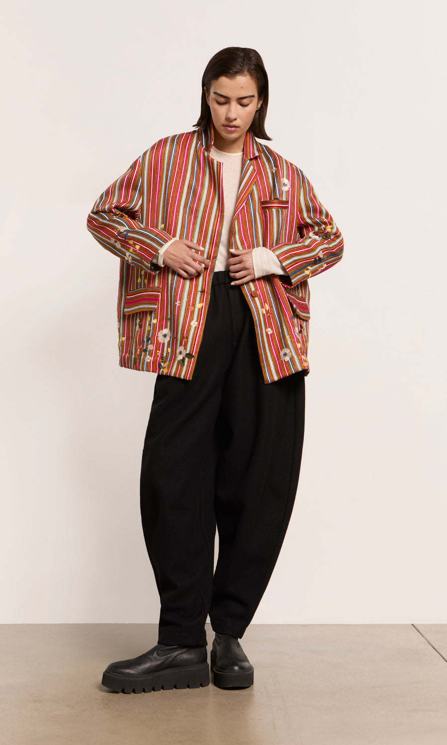 Plümo  A model wears the Masha Blazer with red stripes, a cream top, black baggy pants, and chunky black platform shoes.