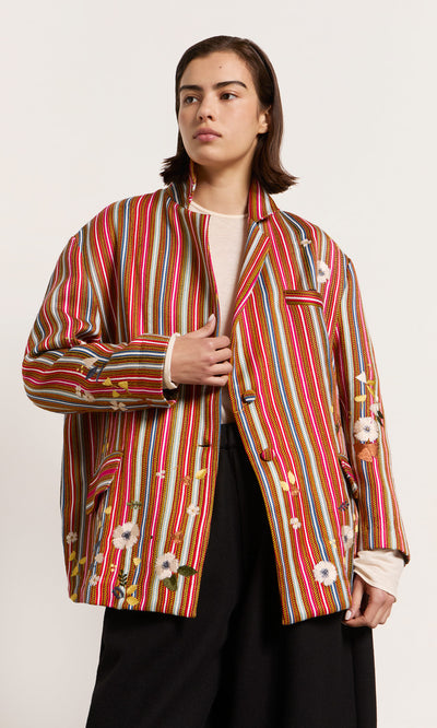 Plümo  A model wears the Masha Blazer with colourful red stripes, embroidered crosses, and flowers over a white top.