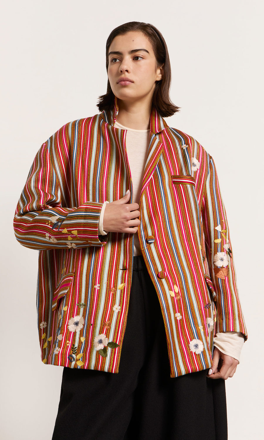Plümo  A model wears the Masha Blazer with colourful red stripes, embroidered crosses, and flowers over a white top.