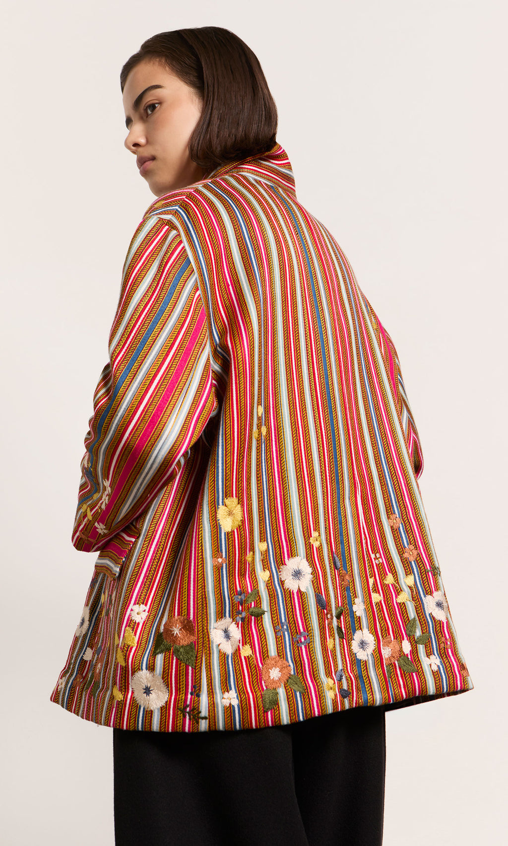 Plümo  Wearing the Masha Blazer with red stripes and hand-stitched flowers, a person glances back over their shoulder.