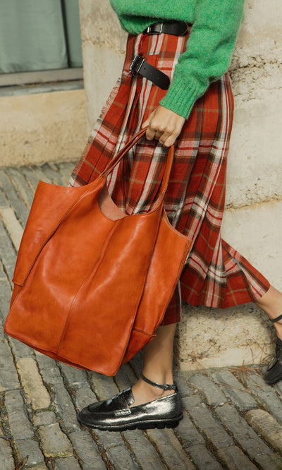 Plümo- Person in a green sweater and plaid skirt carrying the Miller Tote, wearing shiny black shoes.