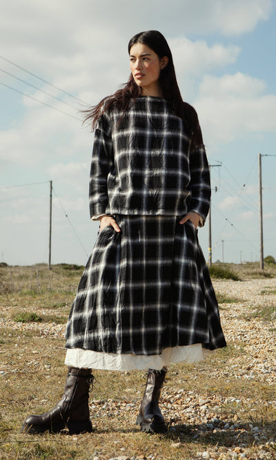 Plümo- A woman in the Gifford Blouse and boots stands outdoors on rocky ground with a cloudy sky behind her.