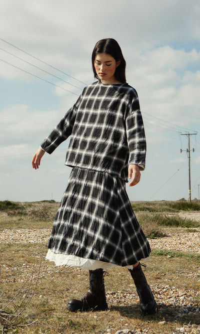 Plümo- A woman wearing the Gifford Blouse and boots stands on grass under a partly cloudy sky.