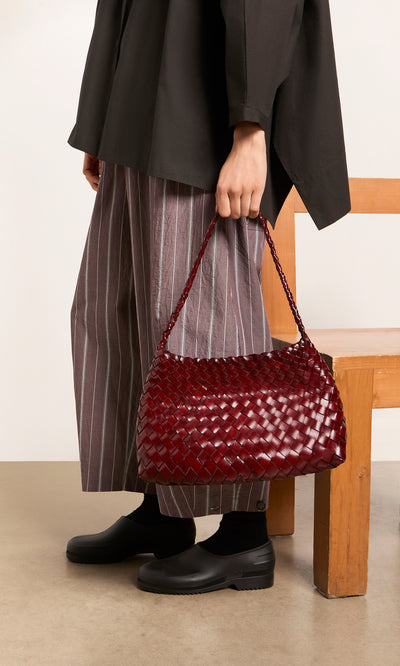 Plümo  Person holding the Moone Bag, wearing wide striped pants, black shoes, and a black top.