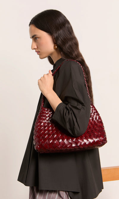 Plümo  A woman in a black shirt carries the Moone Bag, a hand-woven leather purse, over her shoulder.