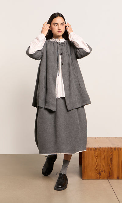 Plümo  Woman in the Moy Jacket and skirt with a white blouse, indoors adjusting her hair.