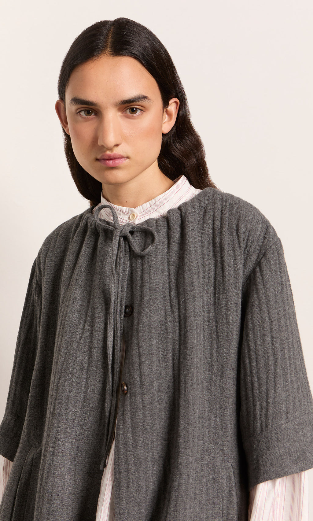 Plümo  Person with long dark hair in the Moy Jacket over a light collared shirt, looking at the camera.