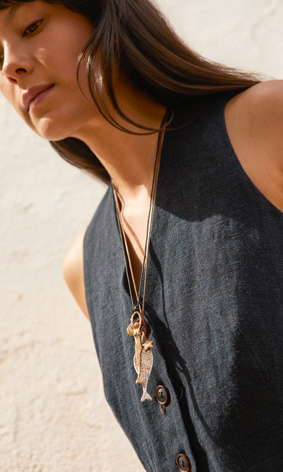 Plümo- Woman in a sleeveless dark dress wearing two Capri Necklaces with ocean charms, standing outdoors.