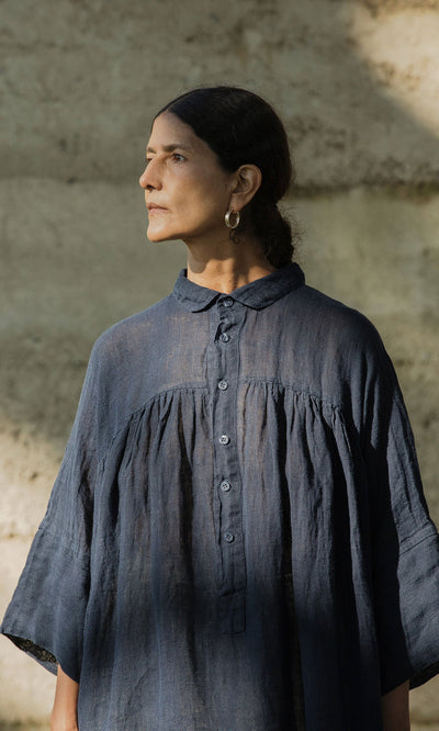 Plümo- A woman in the Thistle Blouse - Deep Navy stands by a textured beige wall, looking to the side.