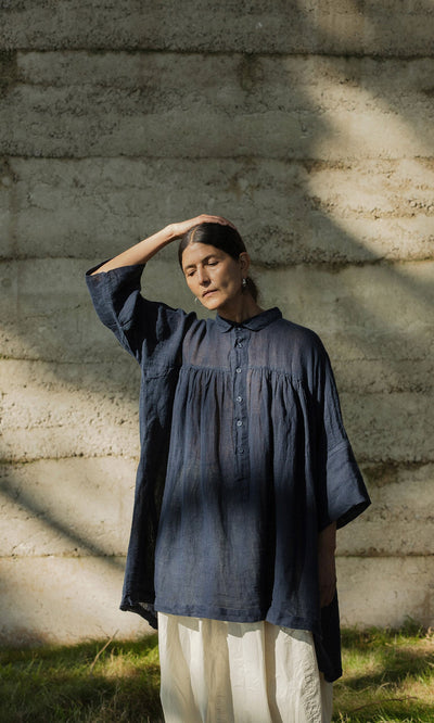 Plümo- A woman in the Thistle Blouse - Deep Navy with cropped sleeves stands, eyes closed, by a sunlit concrete wall.
