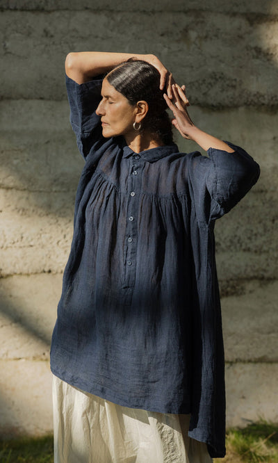 Plümo- A woman in the Thistle Blouse - Deep Navy stands in sunlight, eyes closed, hands on head.