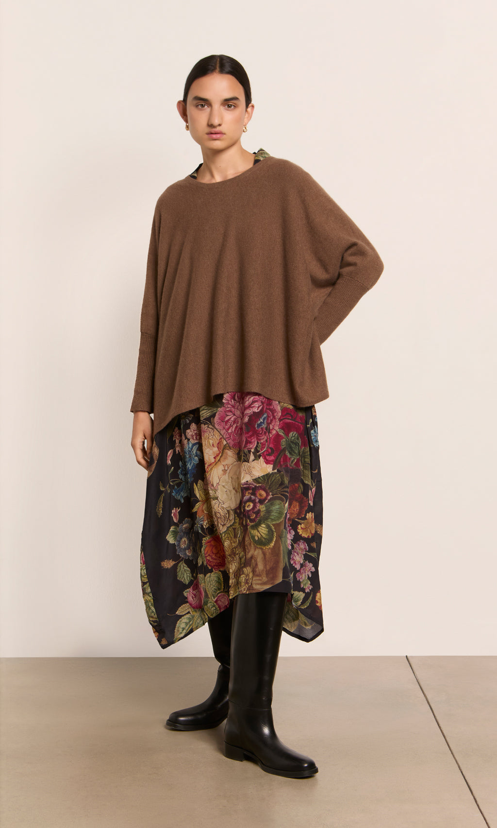 Plümo  Woman wears a cumin Neves Crew Neck, floral skirt, and black knee-high boots against a plain background.