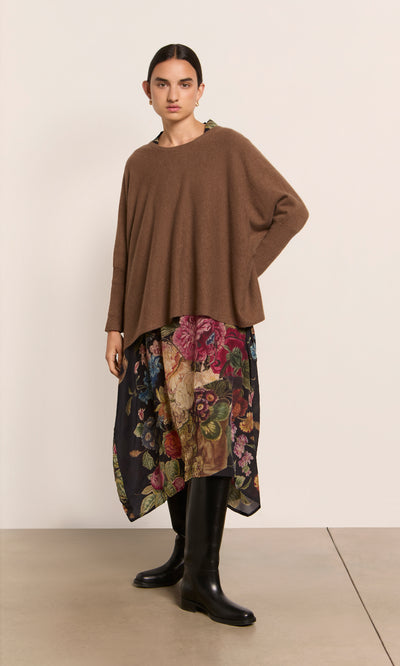 Plümo  Woman wears a cumin Neves Crew Neck, floral skirt, and black knee-high boots against a plain background.