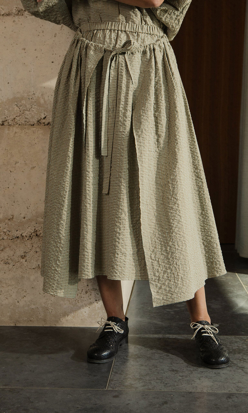 Plümo- Someone wearing the Nori Wrap Skirt, a textured seersucker skirt with a drawstring waist, and black lace-up shoes.