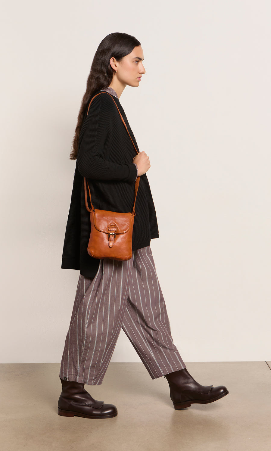 Plümo  Woman in black sweater, striped pants, dark boots, and Parcel Bag - Chestnut against a neutral background.