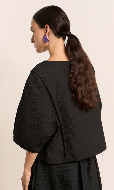 Plümo  Woman with long brown hair in a low ponytail, wearing the Poko Top and purple earrings, facing sideways.