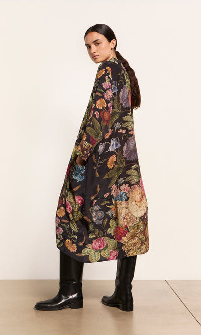 Plümo  Woman in the Primula Dress with an A-line silhouette and black boots stands sideways against a plain background.