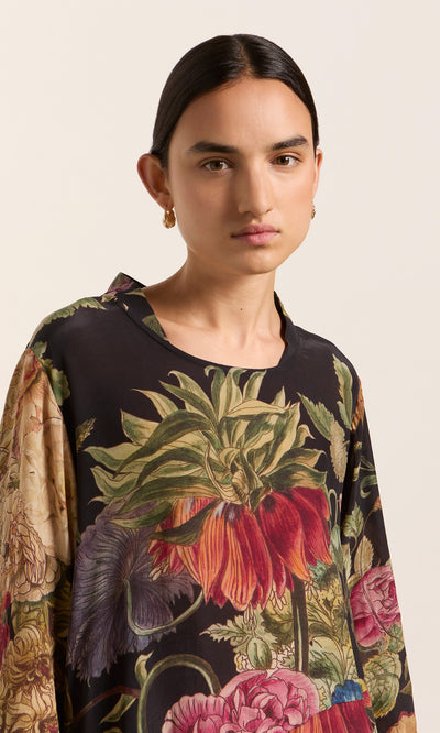 Plümo  Dark-haired person in the Primula Dress against a light background, looking directly at the camera.
