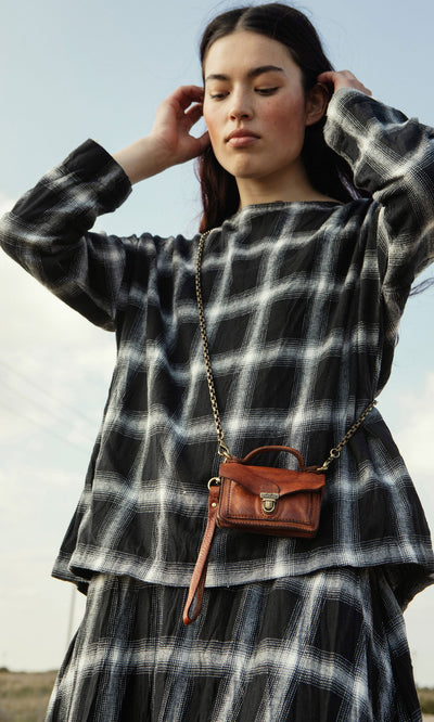 Plümo- Woman in a Gifford Blouse with a small brown crossbody purse, standing outdoors.